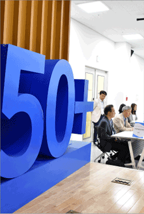 서울시50플러스재단 행사장 전경. 왼쪽에 파란색 대형 '50+' 입체 조형물이 설치되어 있고, 오른쪽에는 참석자들이 테이블에 앉아 행사에 참여하고 있다.